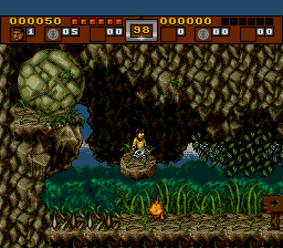 A ninja perched on a rock in a jungle cavern, a huge boulder poised above and vines strung across the gap below